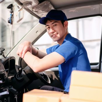 A man in a blue shirt is driving a truck. He is smiling and he is enjoying his time behind the wheel